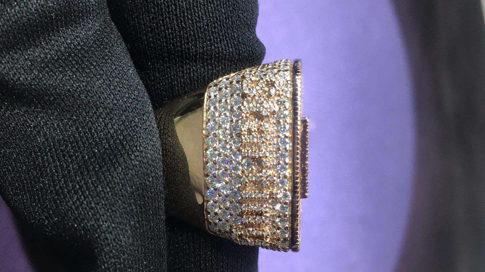 Close-up of a fully iced-out rose gold moissanite ring with a square cushion face, hand-set stones on a black jewelry display