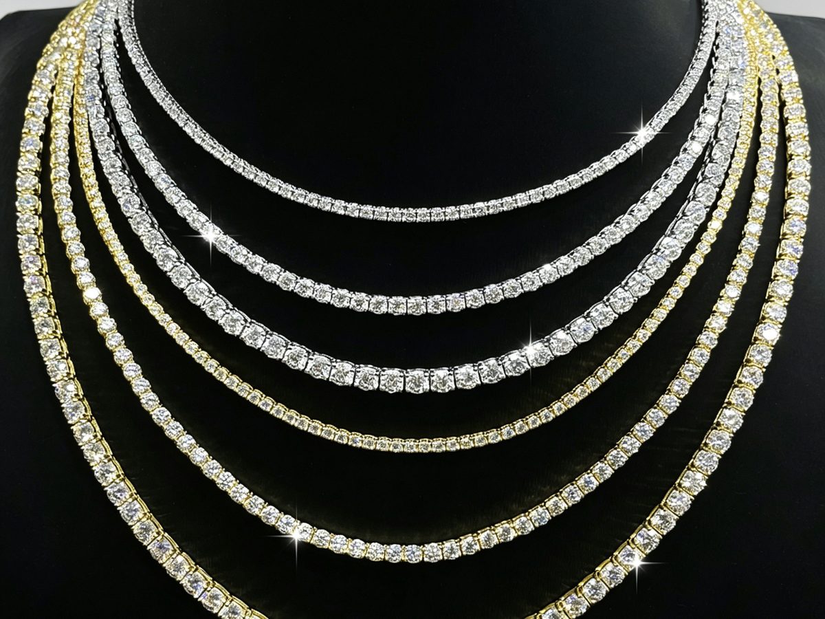 Layered moissanite tennis chains in silver and gold tones on a black display bust, stones individually set in prongs